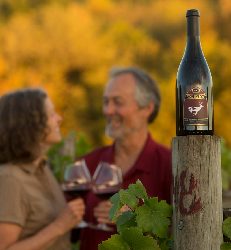Focused bottle of Stag Hollow wine with blurry image of owners in the background